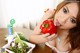 A woman holding a red bell pepper in front of a salad.